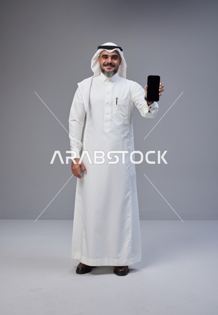رجل سعودي بالزي التقليدي يحمل هاتفاً بشاشة فارغة
