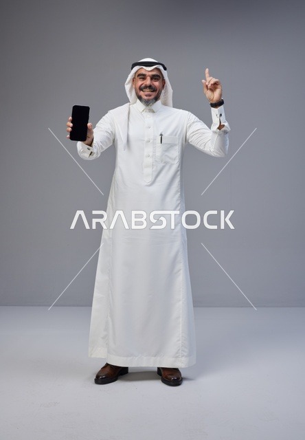 رجل سعودي بالزي التقليدي يحمل هاتفاً ذكياً
