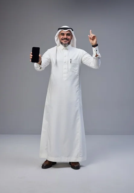 رجل سعودي يحمل هاتفاً بشاشة فارغة على خلفية رمادية