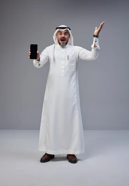 رجل سعودي يحمل هاتف ذكي بشاشة فارغة خلفية رمادية