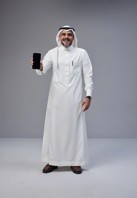 رجل سعودي بالزي التقليدي يحمل هاتفاً بشاشة فارغة