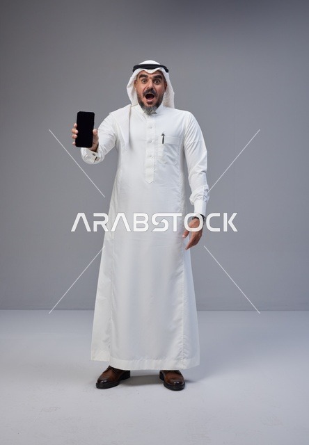Shocked Saudi Man Holding Blank Screen Smartphone in Studio