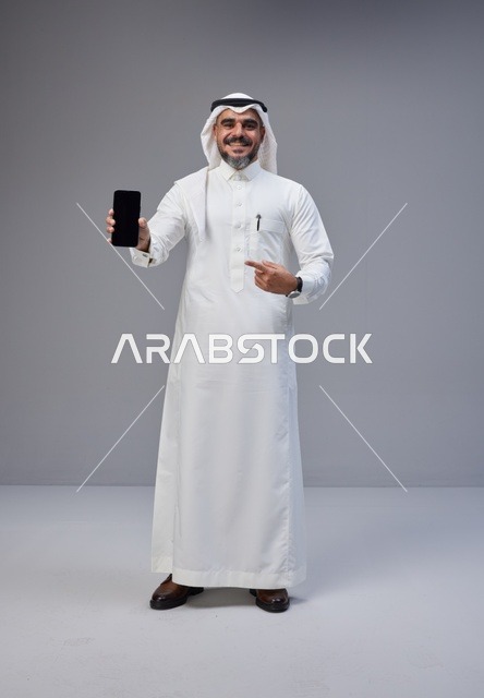 Saudi Man in Thobe Holding Smartphone with Blank Screen