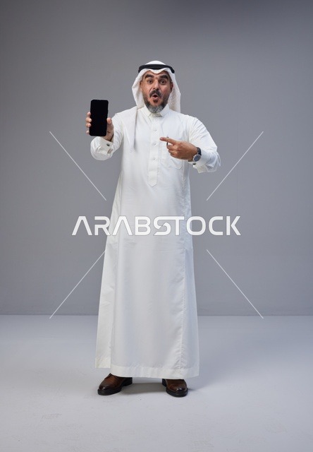 Saudi Man Pointing at Blank Smartphone Screen on Grey