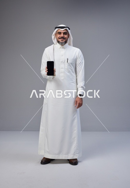 Saudi Man in Traditional Thobe Holding Blank Smartphone