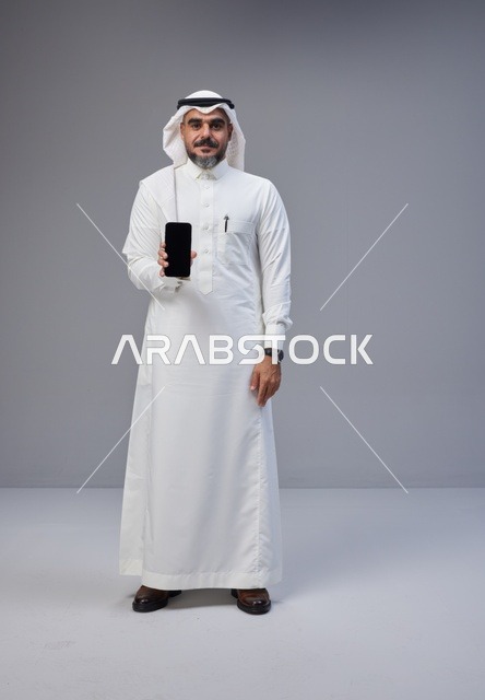 رجل سعودي يحمل هاتفاً بشاشة فارغة