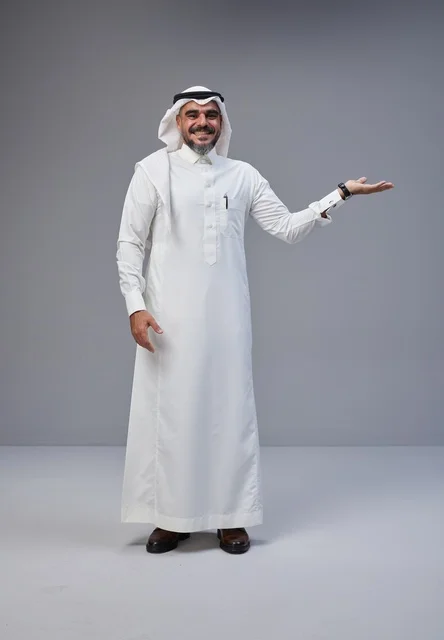 رجل سعودي بالزي التقليدي يشير بيده بخلفية رمادية