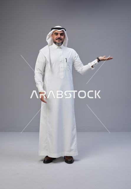 رجل سعودي بالزي التقليدي يشير بيده على خلفية رمادية