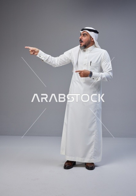 رجل سعودي مندهش يشير للجانب بالزي التقليدي