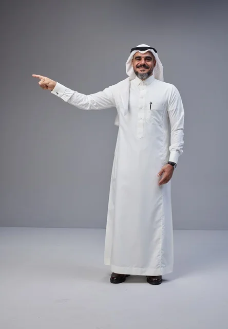 رجل سعودي بالزي التقليدي يشير بيده على خلفية رمادية