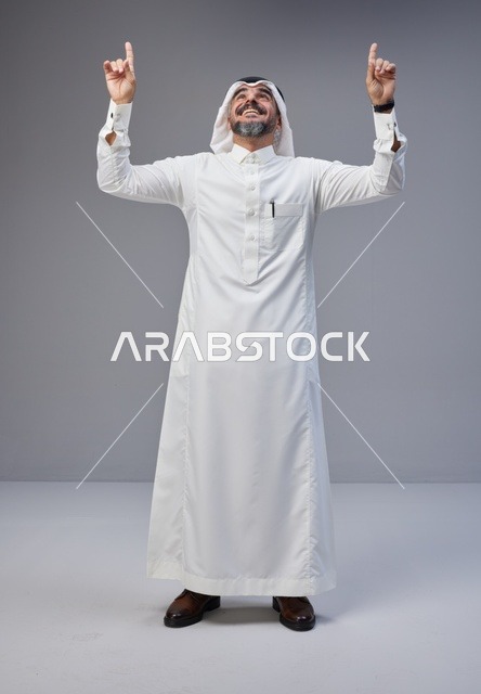 رجل سعودي بالزي التقليدي يشير للأعلى بابتسامة