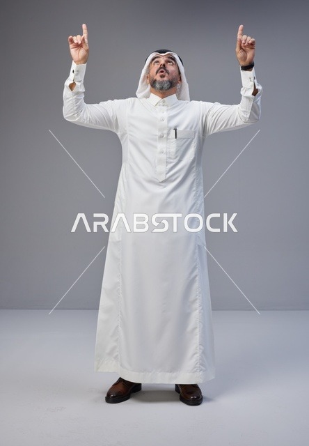 رجل سعودي بالزي التقليدي يشير إلى الأعلى في الاستوديو