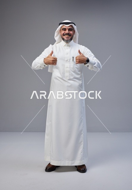رجل سعودي مبتسم بالزي التقليدي يرفع إبهامه في الاستوديو