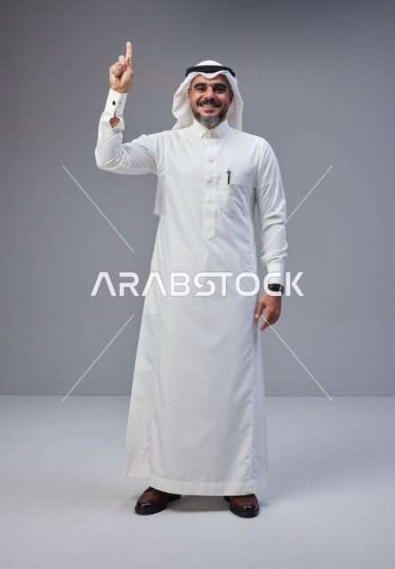 رجل سعودي بالزي التقليدي يشير للأعلى في استوديو