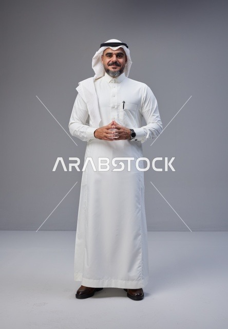 رجل سعودي بالزي التقليدي أمام خلفية رمادية