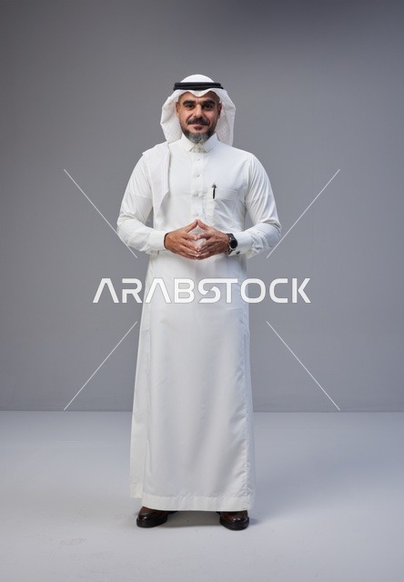 رجل سعودي بالزي التقليدي أمام خلفية رمادية