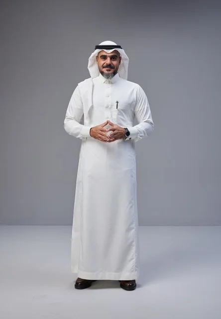 رجل سعودي بالزي التقليدي أمام خلفية رمادية