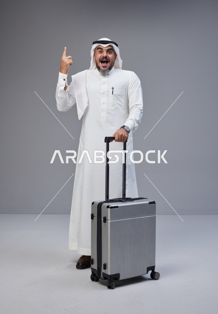 رجل سعودي مع حقيبة سفر يشير للأعلى في استوديو