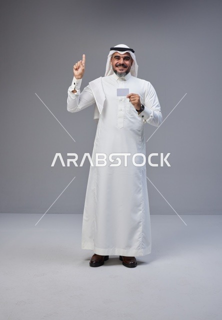 رجل سعودي يحمل بطاقة فارغة ويشير للأعلى في استوديو