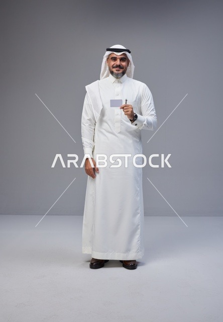 رجل سعودي يحمل بطاقة تعريف فارغة أمام خلفية رمادية