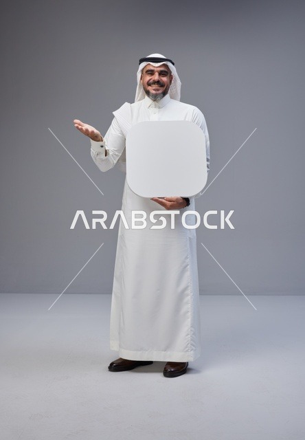 رجل سعودي يحمل لوحة فارغة أمام خلفية رمادية
