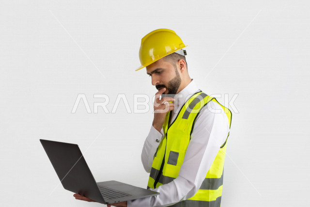 مهندس معماري عربي سعودي  ، استخدام الكمبيوتر المحمول ، رجل  انشاءات باللباس السعودي ، خوذة المهندس ،خلفية بيضاء