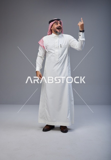 Saudi Man in Traditional Thobe Pointing Up in Studio