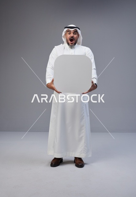 رجل سعودي يحمل لوحة بيضاء فارغة بتعبيرات وجه مندهشة