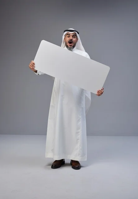 رجل سعودي يرتدي الزي التقليدي يحمل لوحة بيضاء فارغة