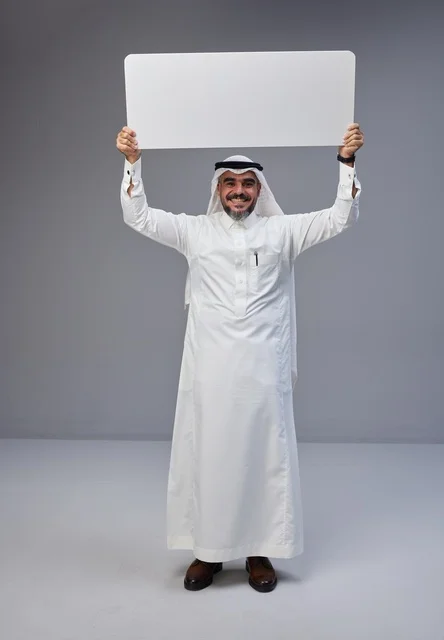 رجل سعودي بالزي التقليدي يحمل لافتة بيضاء فارغة