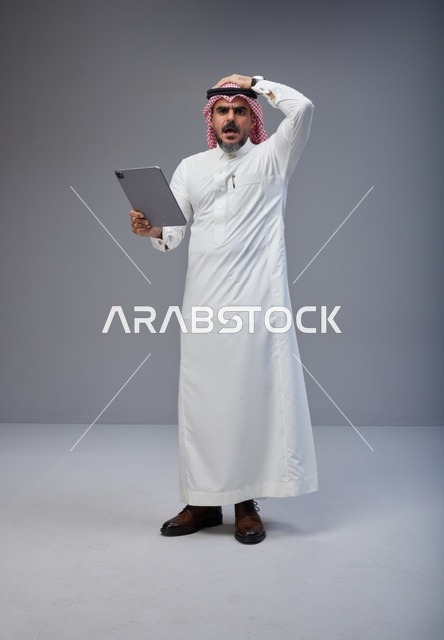 رجل سعودي متفاجئ يحمل جهاز لوحي في الاستوديو