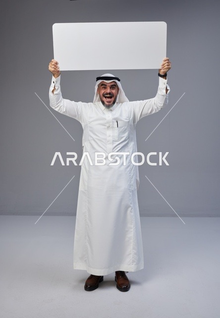 رجل سعودي يحمل لوحة بيضاء فارغة في تصوير استوديو