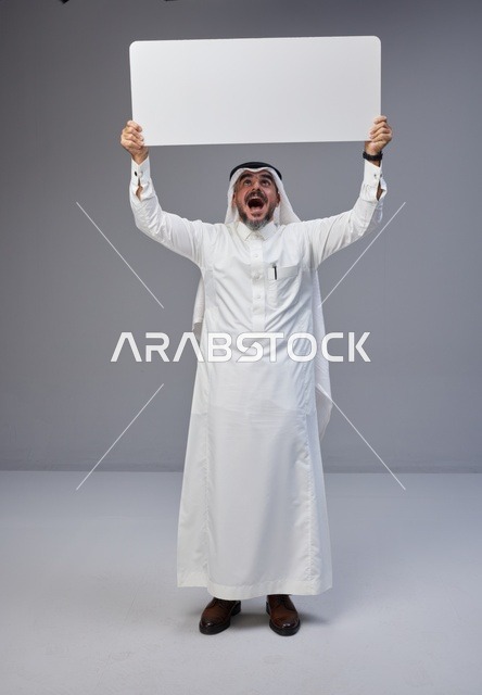 رجل سعودي متحمس يحمل لوحة بيضاء فارغة في استوديو تصوير