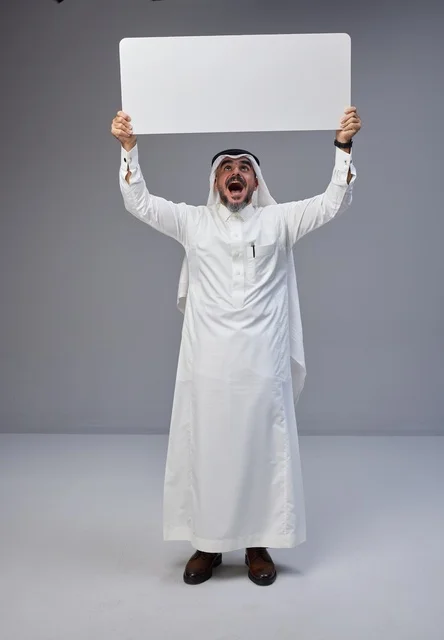 رجل سعودي متحمس يحمل لوحة بيضاء فارغة في استوديو تصوير