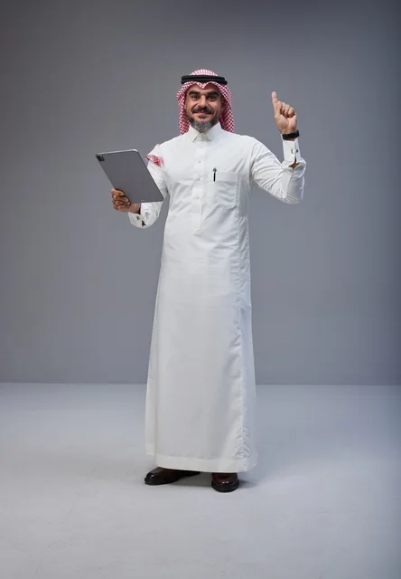 رجل سعودي مع جهاز لوحي يشير للأعلى في استوديو