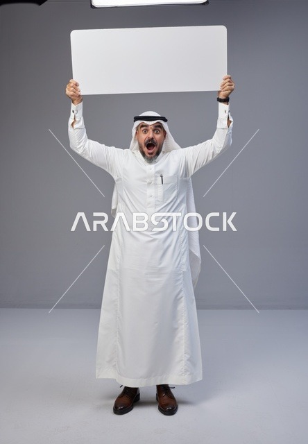 رجل سعودي يحمل لوحة بيضاء فارغة في استوديو