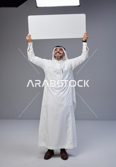 رجل سعودي يحمل لوحة بيضاء فارغة في الاستوديو