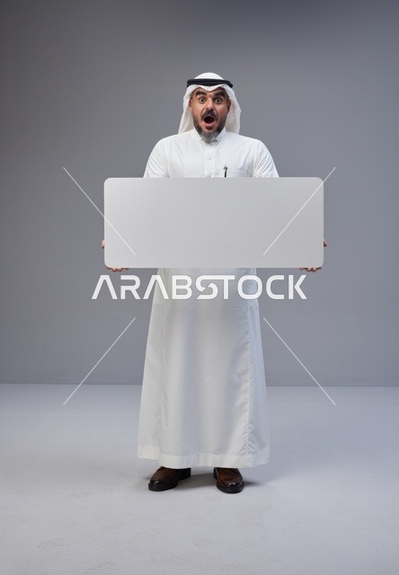 رجل سعودي يحمل لوحة بيضاء فارغة بتعبيرات مندهشة