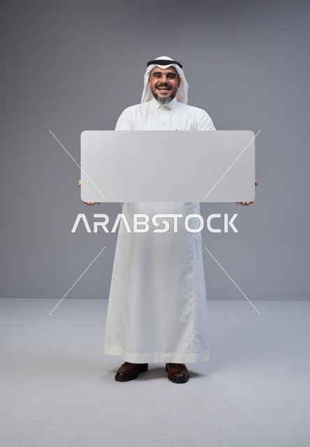 رجل سعودي يحمل لوحة بيضاء فارغة في استوديو