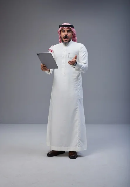 رجل سعودي يحمل جهاز لوحي بتعبير وجه مصدوم