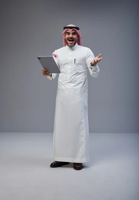 رجل سعودي بالزي التقليدي يستخدم جهاز لوحي بحماس