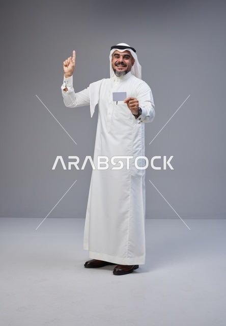 رجل سعودي يحمل بطاقة فارغة ويشير للأعلى خلفية رمادية