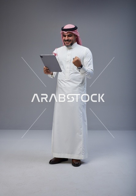 Saudi Man in Traditional Thobe with Tablet Celebrating in Studio