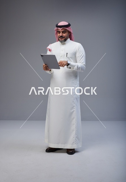 رجل سعودي بالزي التقليدي يستخدم جهاز لوحي