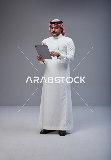 رجل سعودي بالزي التقليدي يستخدم جهاز لوحي