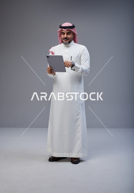 Saudi Man in Traditional Thobe Using Tablet