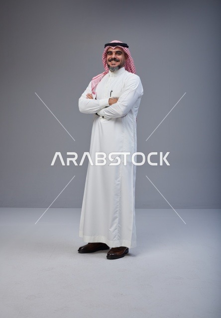 رجل سعودي بالزي التقليدي يقف مكتوف اليدين في الاستوديو