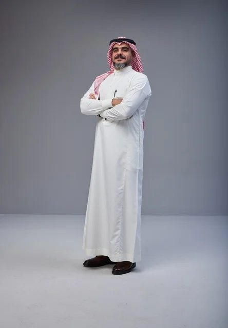 رجل سعودي بالزي التقليدي يقف بثقة بوضعية تقاطع اليدين