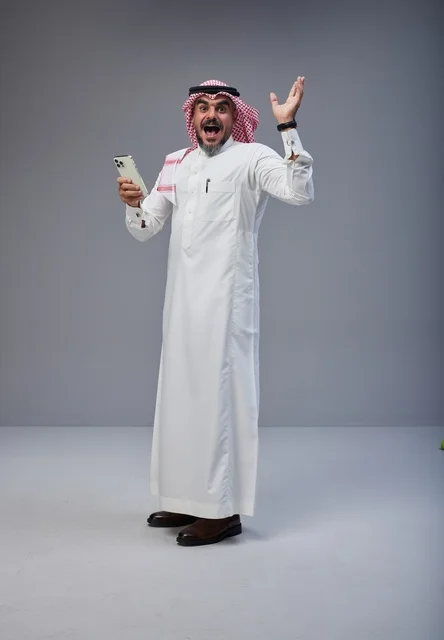 Saudi man in traditional attire using smartphone while walking