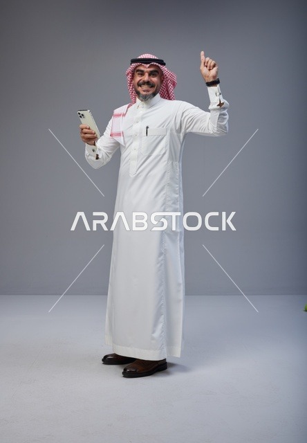 Saudi Man in Thobe Pointing Up with Smartphone
